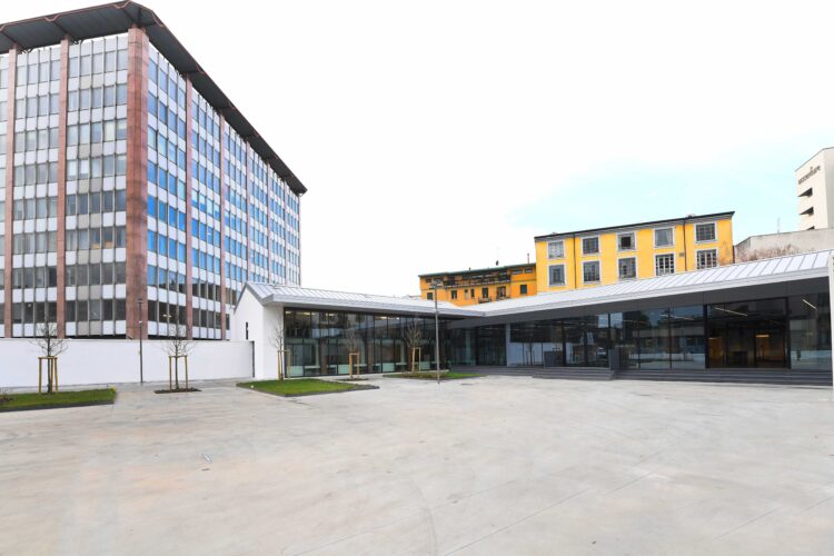 Vista esterna dello spazio eventi moderno, circondato da edifici urbani e un'ampia area aperta.