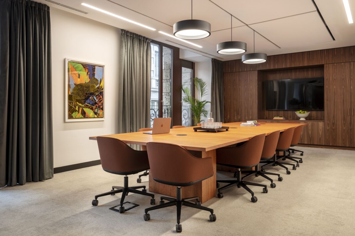 Sala riunioni elegante con tavolo in legno, sedute marroni e tende oscuranti.