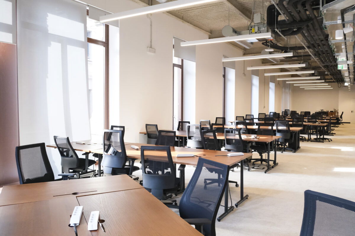 Spazio open space con postazioni di lavoro, scrivanie in legno e sedie ergonomiche nere.