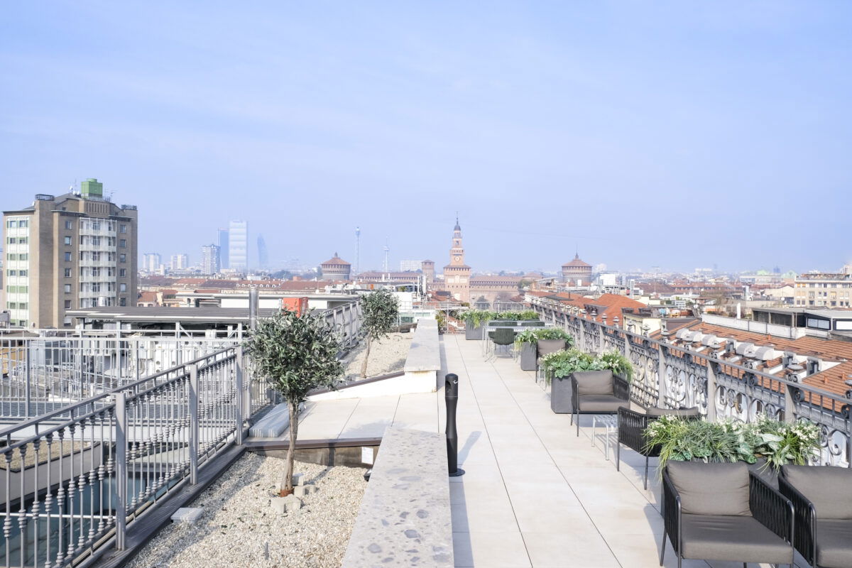 Rooftop panoramico con sedute e piante, vista sul Castello Sforzesco e skyline di Milano.
