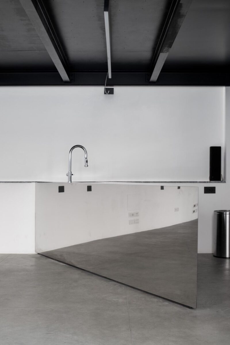 Dettaglio di un bancone bar a specchio con rubinetto cromato in uno spazio minimale.
