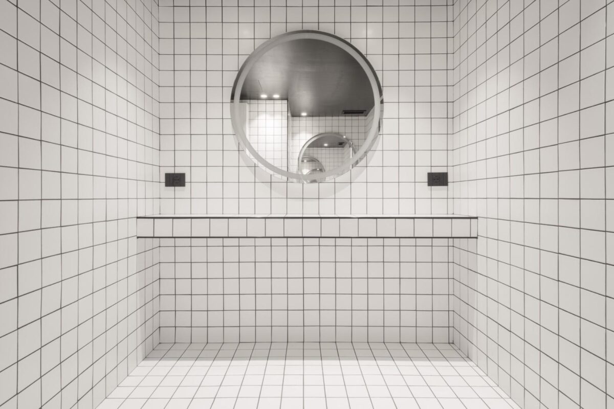 Ambiente moderno con scaffalature in metallo, specchi circolari e pavimento in resina grigia.