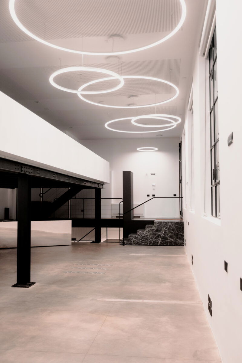 Vista dall'alto su un loft con soffitto bianco, lampade circolari sospese e pareti finestrate.