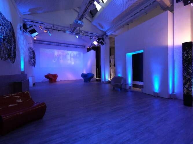 Sala con luci blu, sedute eccentriche e impianto luci su americana per eventi e proiezioni.