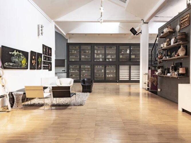 Loft con parquet, quadri e scaffali espositivi, arredato con sedie moderne e tappeto centrale.
