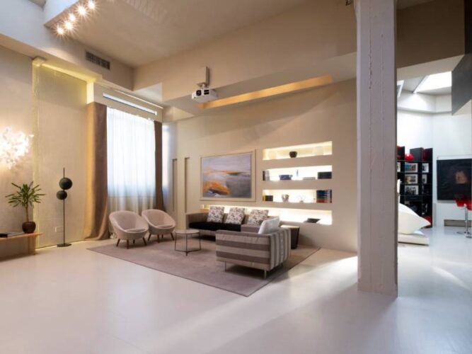 Area living luminosa con divani chiari, parete attrezzata retroilluminata e quadro decorativo.