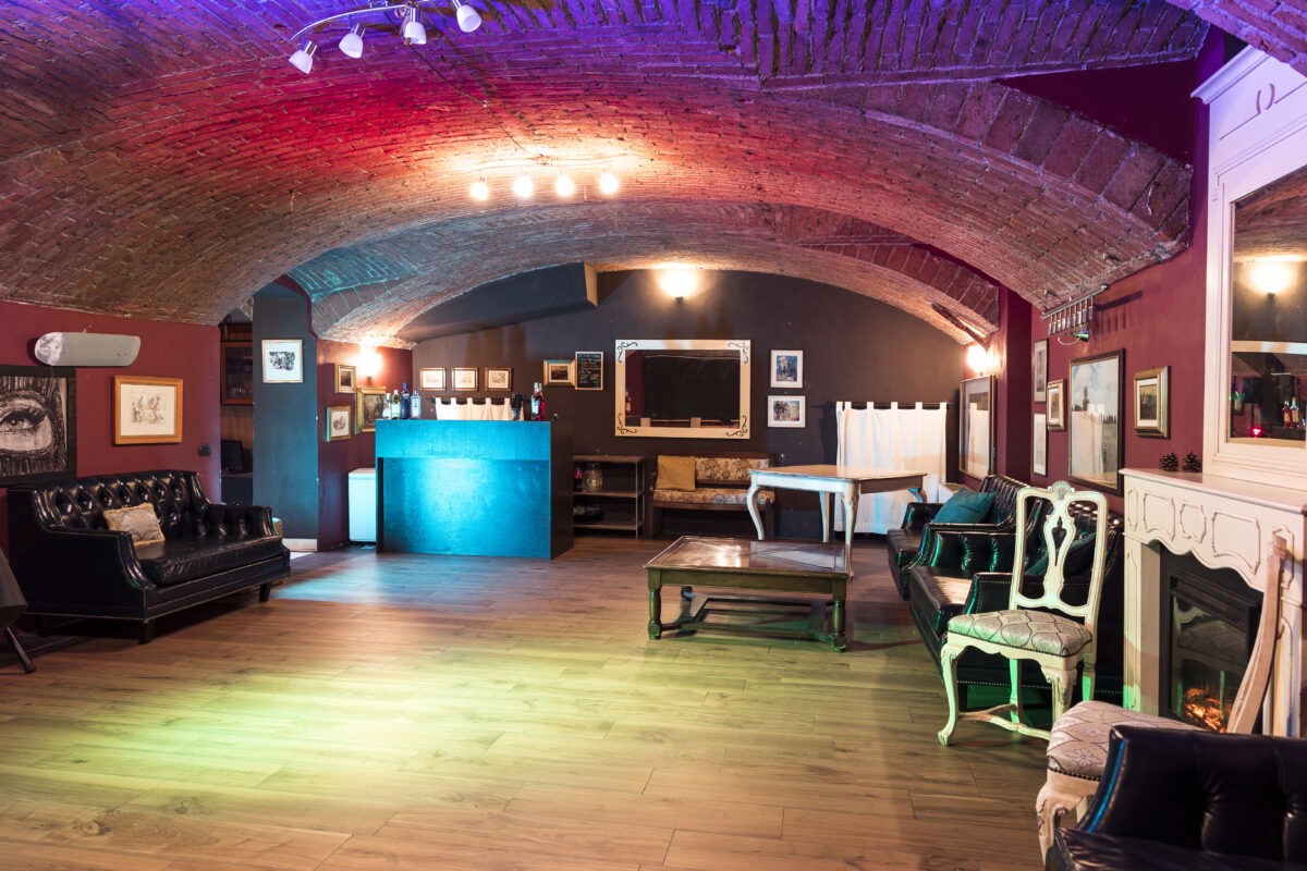 Spazio eventi interno con volte in mattoni, divani vintage e bancone bar