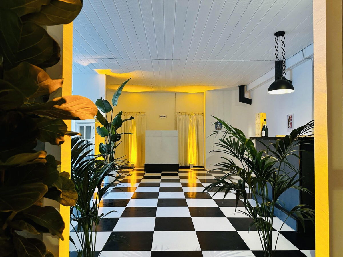 Zona bar di Loft Eventi Gorla con postazione dj, luci calde e decorazioni vegetali su fondo total white